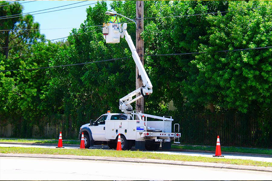 Specialized Business Insurance - White Truck with Lift Lifting Up a Person to Fix Electrical Wires on a Pole Outside